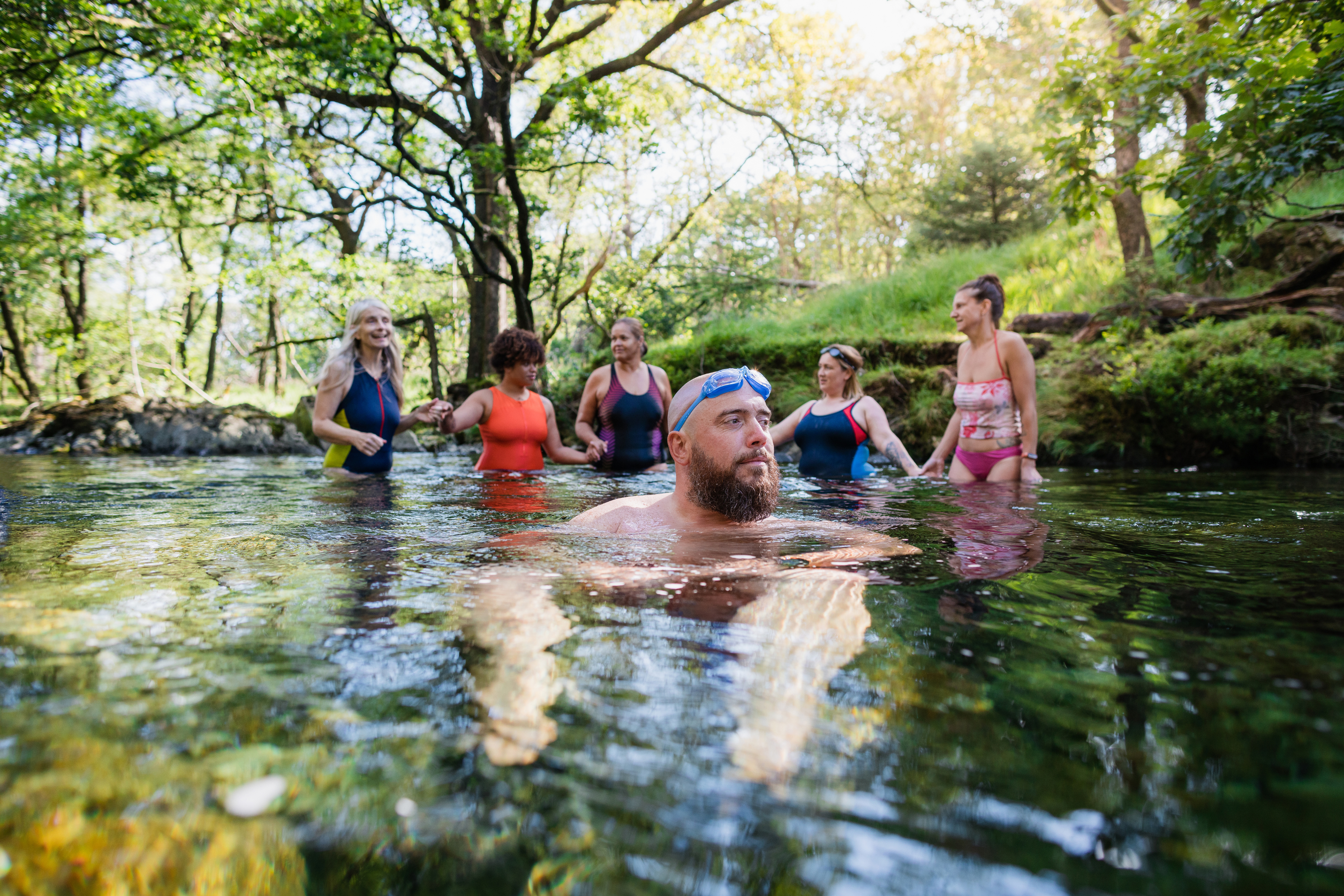 Group of friends enjoying wild swimming in woodland river